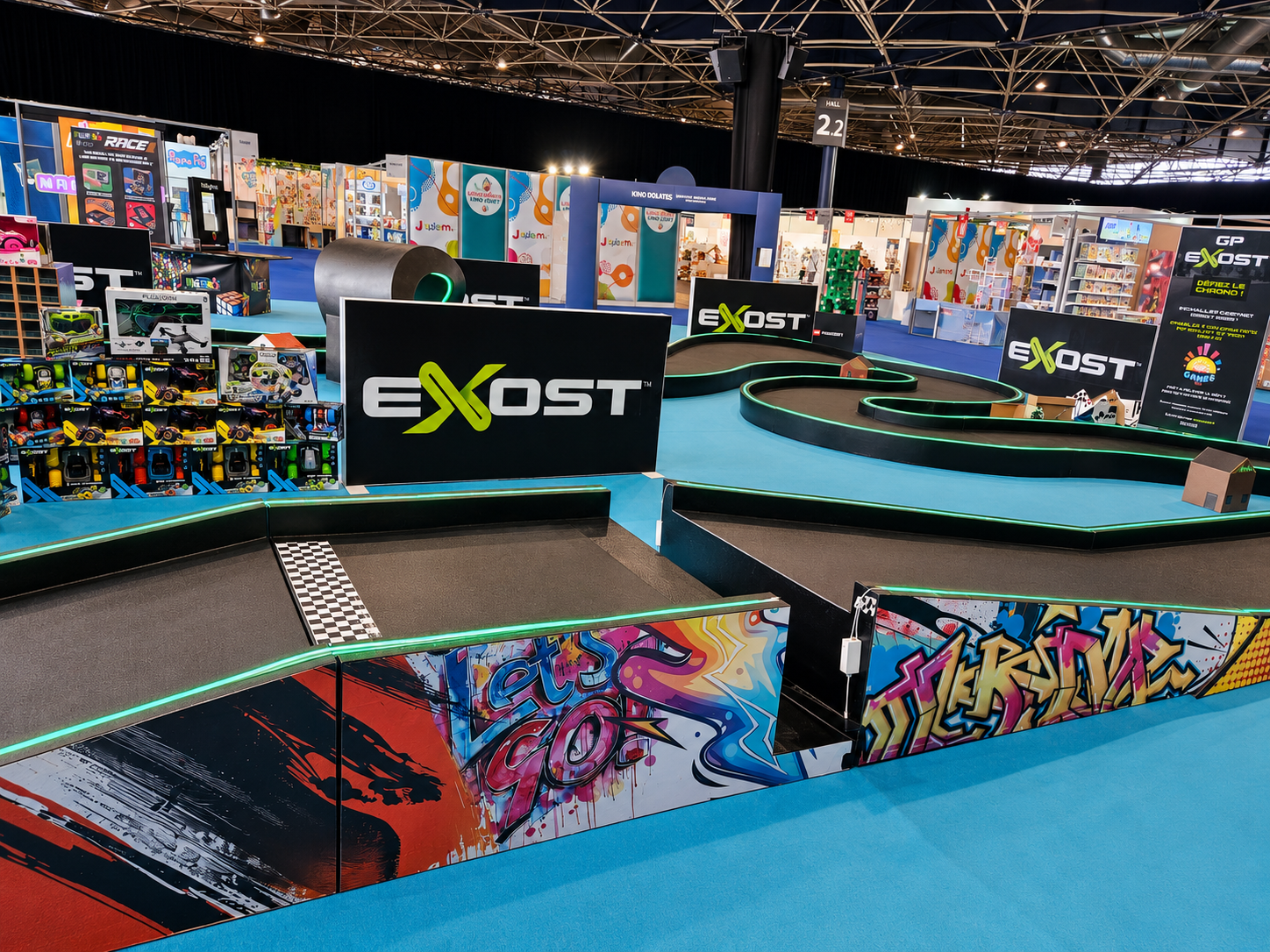 Circuit XL Exost pour voitures radio-télécommandées avec ligne d’arrivée, tubes LED verts, panneaux de marque et décors sur salon du jouet.